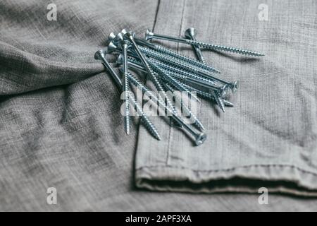 Eine Handvoll metallischer Selbstschneiderschrauben liegt vor dem Hintergrund eines alten Denimstoffs. Selektives Fokusmakro mit flachem Freiheitsgrad. Stockfoto