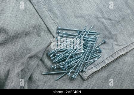 Eine Handvoll metallischer Selbstschneiderschrauben liegt vor dem Hintergrund eines alten Denimstoffs. Selektives Fokusmakro mit flachem Freiheitsgrad. Stockfoto
