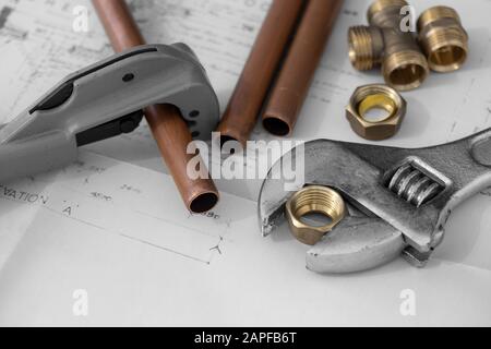 Kupferrohrschneider und verstellbare Schraubenschlüsselwerkzeuge auf einer Reihe von Architektur-Bauplänen mit Rohrleitungsanschlüssen. Selektive Farbe Stockfoto