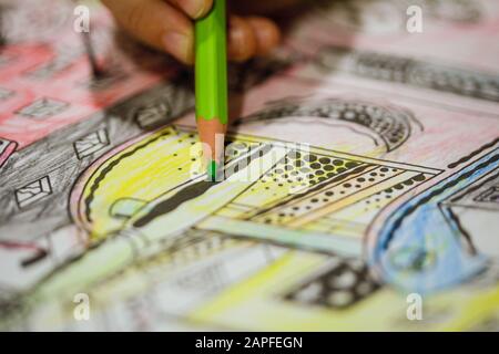 Geringe Schärfentiefe (selektiver Fokus) und Makrobild mit der Hand eines kleinen Mädchens mit einem farbigen Bleistift zum Zeichnen eines Farbbuchs. Stockfoto