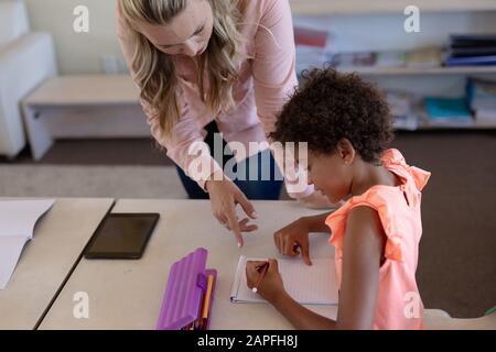 Lehrerin mit langen blonden Haaren hilft einem Schulmädchen in einem Klassenzimmer Stockfoto