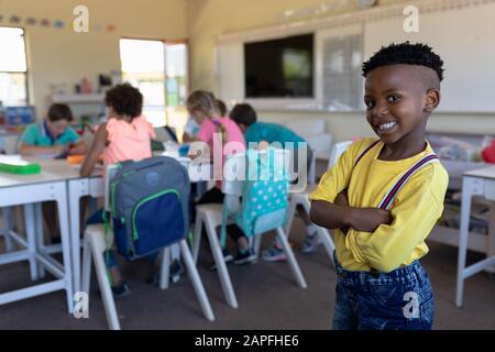 Mit Armen stehende Schulkinder in einem Schulklassenzimmer der Grundschule Stockfoto