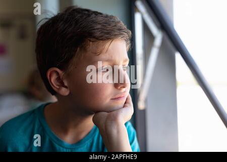 Schuljunge, der aus einem offenen Fenster in einem Schulklassenzimmer schaut Stockfoto