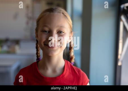 Schulmädchen mit blonden Haaren in Zöpfen, die in einem Grundschul-Klassenzimmer zur Kamera schauen Stockfoto