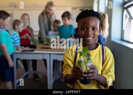 Der Schuljunge, der in einem Erdkrug in einem Klassenzimmer der Grundschule eine Säbelanlage hält Stockfoto