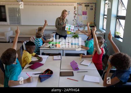 Lehrerin und eine Gruppe von Schulkindern, die an Schreibtischen in einem Schulunterricht sitzen Stockfoto