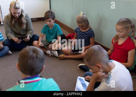 Schullehrerin, die im Kreis mit einer Gruppe von Schulkindern a auf dem Boden quer gesessen hat Stockfoto