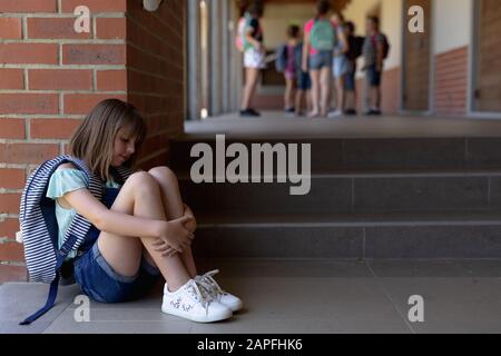 Allein auf dem Schulhof der Grundschule sitzt Schulmädchen auf dem Boden Stockfoto