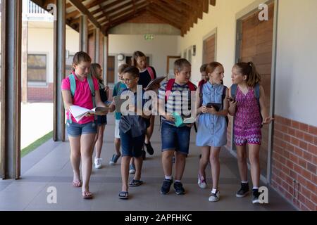 Gruppe von Schülern, die in einem Außenkorridor an der Grundschule spazieren gehen Stockfoto