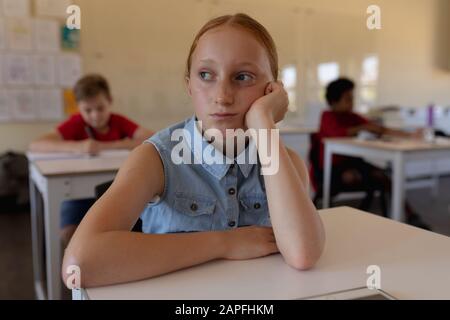 Schulmädchen lehnte sich in einem Schulunterricht auf ihren Schreibtisch Stockfoto