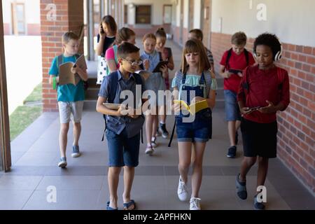 Gruppe von Schülern, die in einem Außenkorridor an der Grundschule spazieren gehen Stockfoto