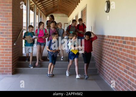 Gruppe von Schülern, die in einem Außenkorridor an der Grundschule spazieren gehen Stockfoto