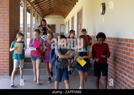 Gruppe von Schülern, die in einem Außenkorridor an der Grundschule spazieren gehen Stockfoto