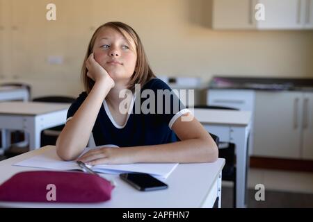 Schulmädchen sitzt an einem Schreibtisch in einem leeren Schulzimmer Stockfoto