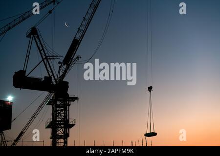 Silhouette der Konstruktion Turmkräne, die Baumaterialien während des Sonnenuntergangs anheben - Hebebeton für Industriekran bei der Entwicklung von Wolkenkratzers in der Stadt - Immobilien, Entwicklung und Wohnblock Stockfoto