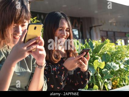 Junge, tausendjährige asiatische Freunde, die im Freien Instant Messaging auf Smartphones nutzen - Fröhliche lächelnde Mädchen, die mit dem Handy in sozialen Medien chatten - Konzept Für Freizeit, Lifestyle und Pals Stockfoto