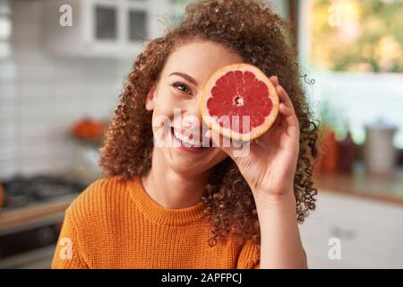 Porträt der Frau, die ihr Auge mit Grapefruit bedeckt Stockfoto