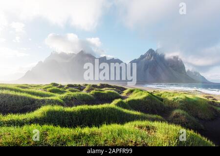 Wunderschöne Landschaft mit schwarzen Sanddünen und grasigen Buchten in der Nähe berühmter Stokksnes Berge am Vestrahorn cape, Island Stockfoto