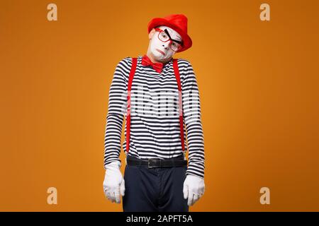 Trauriger MIME in Weste und rotem Hut Isoliert auf orangefarbenem Hintergrund Stockfoto