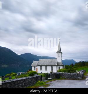 Typische christentumskirche mit Friedhof von Nes Dorf, Pfarrkirche in Luster Gemeinde im Kreis Sogn og Fjordane, Norwegen. Lustrafjord im Hintergrund. Landschaftsfotografie Stockfoto