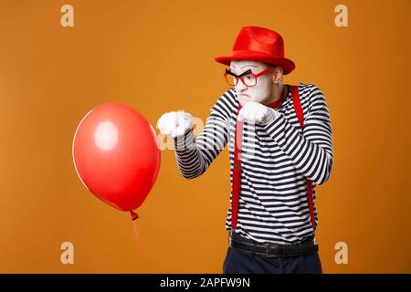 Verärgerter MIME mit rotem Ball auf leerem orangefarbenem Hintergrund Stockfoto