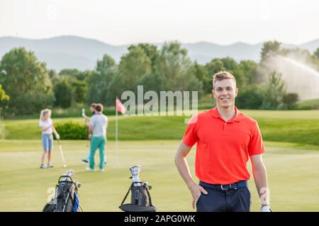 Mann mit Freunden, der im Hintergrund auf dem Golfplatz Golf spielt Stockfoto