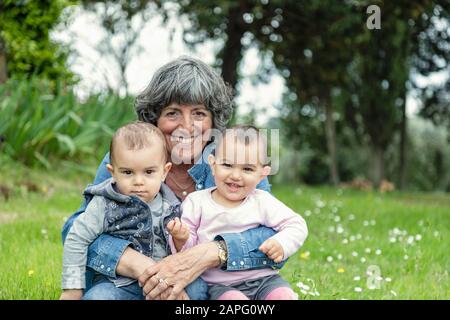 Großmutter mit zwei Enkelkindern auf dem Schoß im Garten, Florenz, Italien Stockfoto