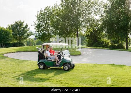 Ein Paar, das auf einem Golfplatz auf einem Buggy reitet Stockfoto