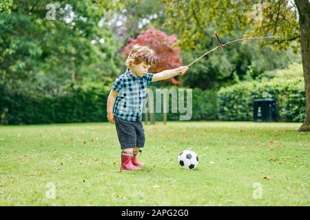 Kleinkind spielt mit Stock und Fußball im Park Stockfoto