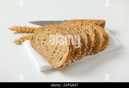 Brotlaib aus Vollkornbrot auf weißer Serviette, Weizenähren und Küchenmesser daneben Stockfoto