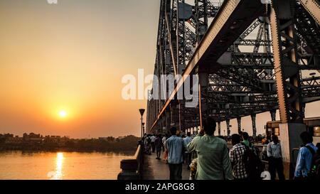 Blick über den Hooghly River an der untergehenden Sonne wie Scharen von Menschen und Verkehr über die Brücke hin und her. Stockfoto