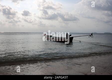 Angedocktes Boot an der Küste unter Wolken bei Sonnenuntergang am Inselstrand von Koh Phangan, Thailand Stockfoto