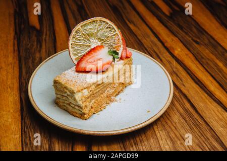 Ein köstliches Stück Honigkuchen wird mit frischen Erdbeeren auf einem Teller serviert, der auf einem Holzhintergrund steht. Stockfoto