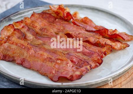 Knuspriger gebratener Speck in einer gusseisernen Pfanne auf grauem Grund. Stockfoto