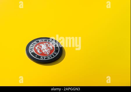 Oldtimer-Logo in der Nähe eines gelben klassischen Austin Healey Sprite Automobils - ca. 1960 in Rushmoor, Großbritannien - 19. April 2019 Stockfoto