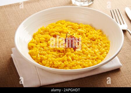 Eine Schale cremig gelber Risotto Reis mit Safranfäden aus der Region Lombardei in Italien wird in einer weißen Schüssel am Tisch serviert Stockfoto