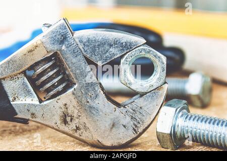 Ein verstellbarer Schraubenschlüssel liegt in der Nähe der Schrauben und Muttern der Unterlegscheibe vor dem Hintergrund von Holzplatten. Das Konzept der Werkzeuge und Reparaturarbeiten. Stockfoto
