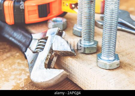 Ein verstellbarer Schraubenschlüssel liegt in der Nähe der Schrauben und Muttern der Unterlegscheibe vor dem Hintergrund von Holzplatten. Das Konzept der Werkzeuge und Reparaturarbeiten. Stockfoto
