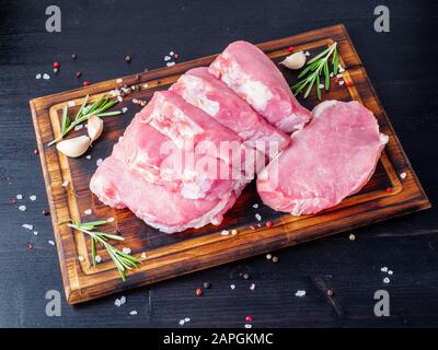 Schweinesteak, rohes Karbonatfilet auf dunklem Hintergrund, Fleisch mit Rosmarin, Gewürze, Seitenansicht Stockfoto