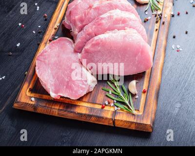 Schweinesteak, rohes Karbonatfilet auf dunklem Hintergrund, Fleisch mit Rosmarin, Gewürze, Seitenansicht Stockfoto