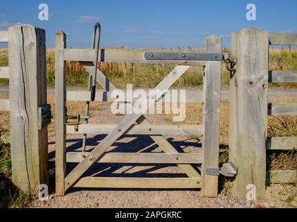 Robustes, bewaldetes Tor und Zaun, mit Fußweg und Feldern im Hintergrund. Medmerry Nature Reserve, ein Hochwasserschutzsystem der Umweltbehörde, West Sussex Stockfoto