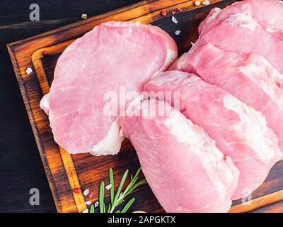 Schweinesteak, rohes Karbonatfilet auf dunklem Grund, Fleisch mit Rosmarin, Stockfoto