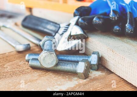 Ein verstellbarer Schraubenschlüssel liegt in der Nähe der Schrauben und Muttern der Unterlegscheibe vor dem Hintergrund von Holzplatten. Das Konzept der Werkzeuge und Reparaturarbeiten. Stockfoto