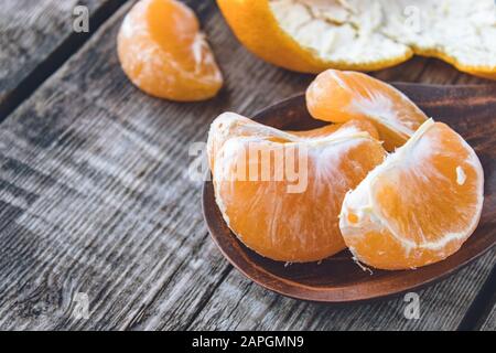 Scheiben von reifen gelben Tangerinen liegen in einer Schüssel nahe der Tangerinschälung auf einem Holztisch. Zitrusfrüchte, Mandarinen oder Orangen. Nahaufnahme. Stockfoto