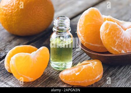 Reife geschälte Scheiben von Tangerin ohne Schale und eine Flasche ätherisches Öl mit Tangerin auf dem Tisch. Zitrusfrüchte, Mandarinen oder Orangen. Alternative Stockfoto