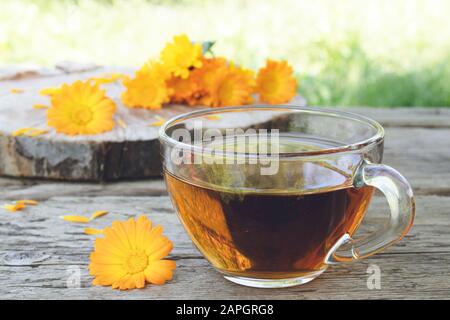 Tasse mit marigalten und kalendulaschen Teeblumen im Freien auf grünem Hintergrund. Extrakt der Tinktur von Calendula im Becher. Heilpflanzen. Stockfoto