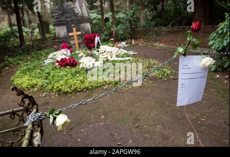 Hamburg, Deutschland. Januar 2020. Blumen liegen auf dem Grab des Schauspielers Jan Fedder auf dem Ohlsdorfer Friedhof. Davor hängt eine Kette mit einem Schild, das sagt: "Ich schlafe. Bitte nicht stören. Lassen Sie Ihre Blumen und Kerzen vorne. Das Zimmer vor dem Mahnmal ist mein Zimmer, nicht betreten!! Ta! Dein Jan'. Um die Pflanzen und den Rasen auf dem Grab des Schauspielers zu schützen, haben Friedhofsmitarbeiter eine Kette vor die Ruhestätte gelegt. (Zu dpa "Zerwürfnis am Fedder Grab - Friedhof legt Zeichen und Kette") Credit: Daniel Bockwoldt / dpa / Alamy Live News Stockfoto