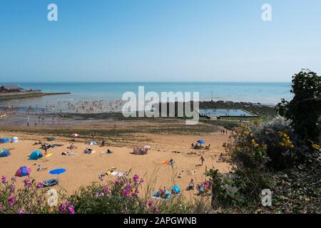 Menschen sonnen sich und Kinder spielen am Strand, natürliches Meerespool in den Felsen an der Viking Bay, Broadstairs, Kent, Großbritannien Stockfoto