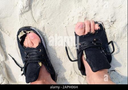 Ein Mann, der alte abgenutzte Schuhe an Füßen mit Löchern trägt Stockfoto