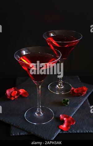 Zwei kosmopolitische Cocktails in einem Dreiecksglas. Vor einem dunklen luxuriösen Hintergrund sind Rosenblätter verstreut. Hohe Auflösung. Stockfoto